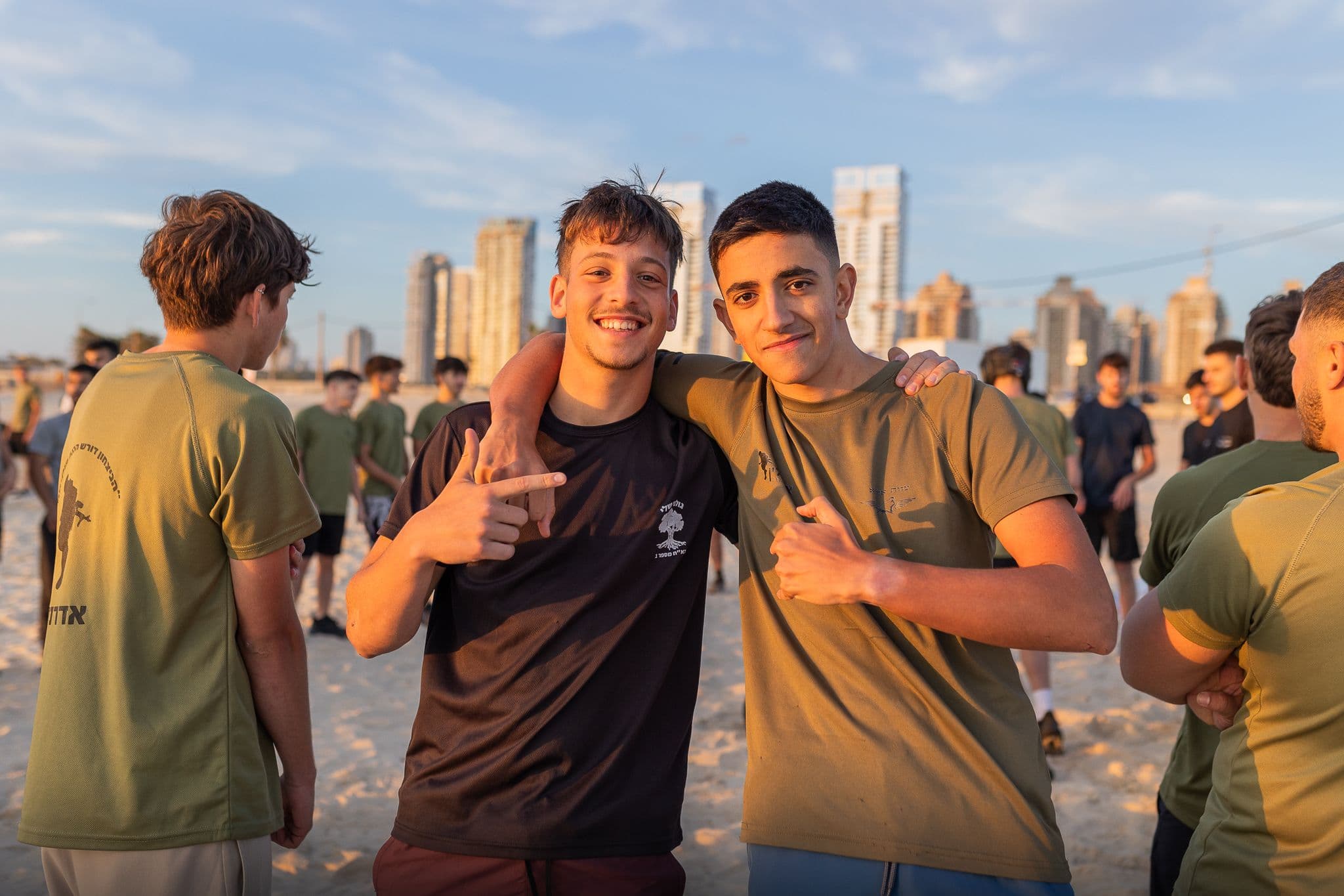שני חניכי אדרנלין מחובקים על החוף, ומאחוריהם בנייני העיר