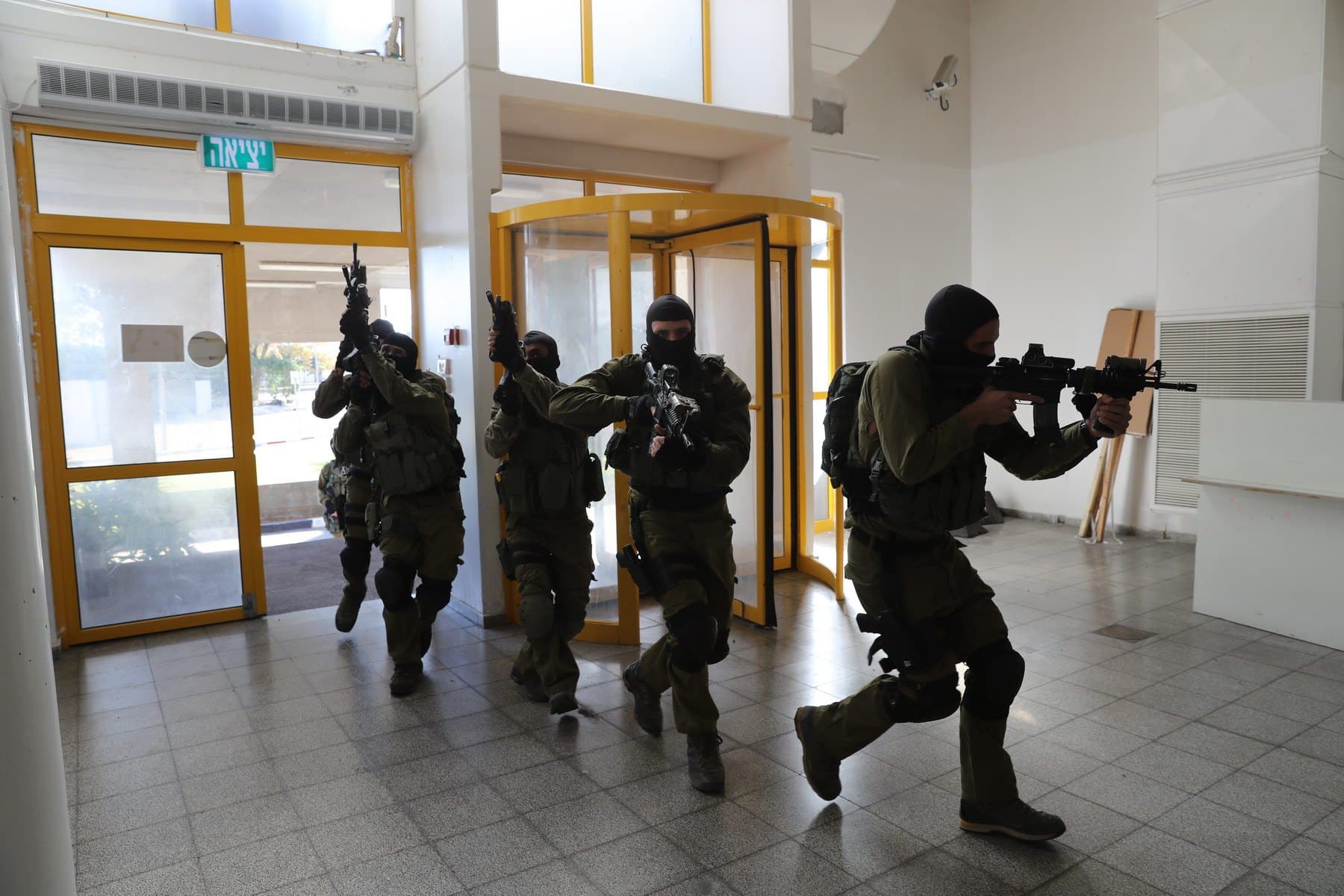 צוות לוחמים נכנס למבנה בתרגיל לחימה בשטח בנוי, נשקים מכוונים קדימה